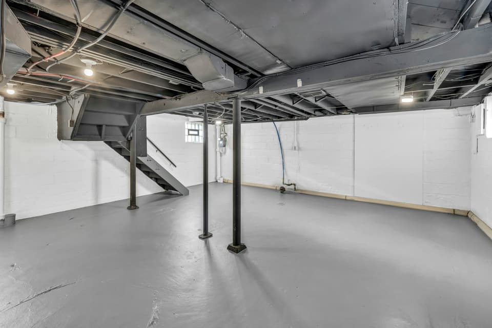 An empty unfinished basement with a painted concrete floor and steel support posts