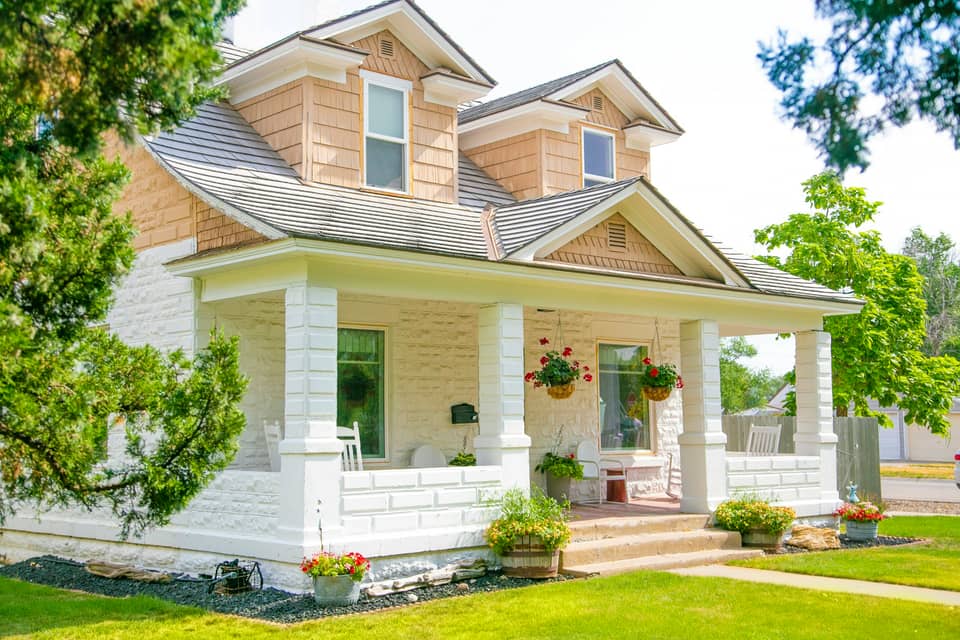 A two-storey house with a deep covered front porch, white columns and hanging flower baskets