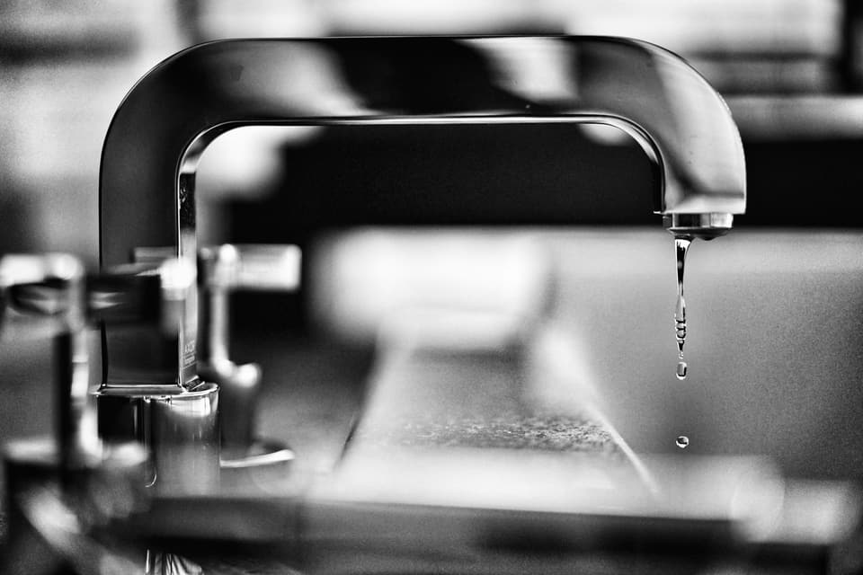 Water dripping from a chrome tap, in black and white